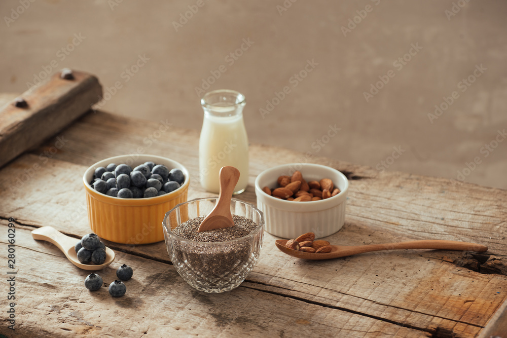 新鲜蓝莓、杏仁和奇亚籽，木板上有牛奶。理想的健康早餐理念。