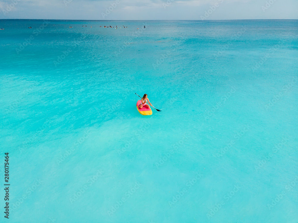 Aerial view of woman on stand up paddle board in blue ocean.