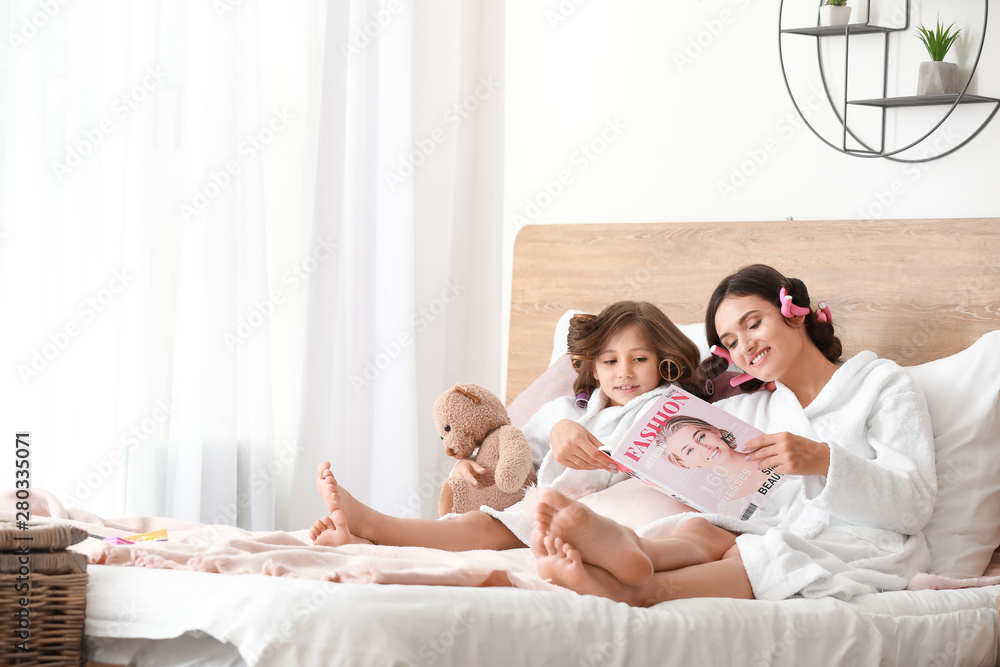Mother and her little daughter in bathrobes and with fashion magazine relaxing at home