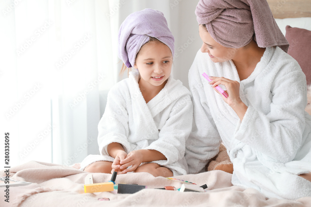 Mother and her little daughter in bathrobes manicuring nails in bedroom