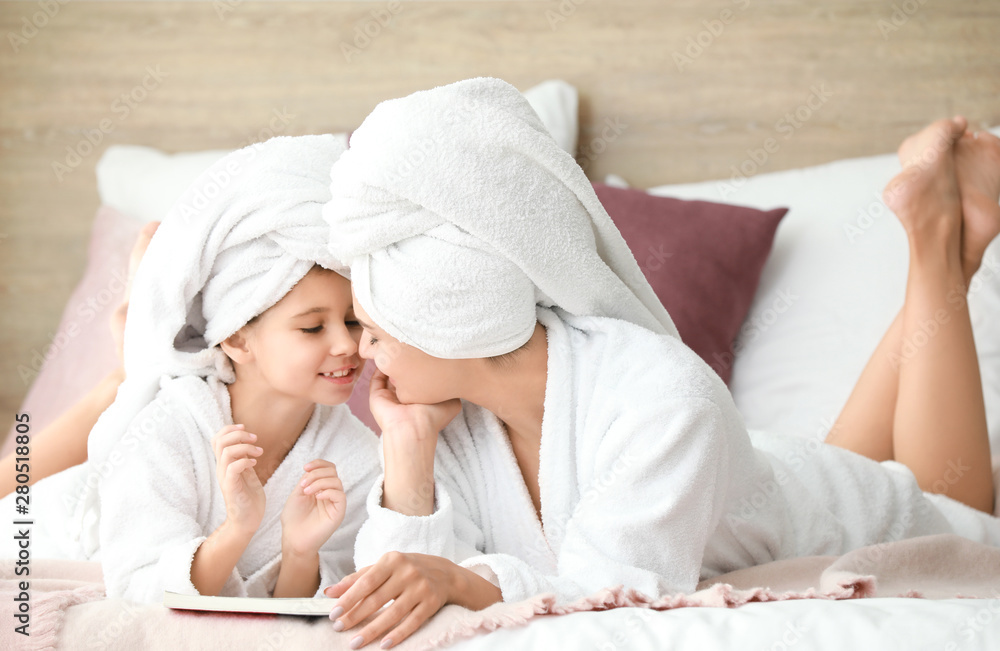 Mother and her little daughter in bathrobes relaxing in bedroom