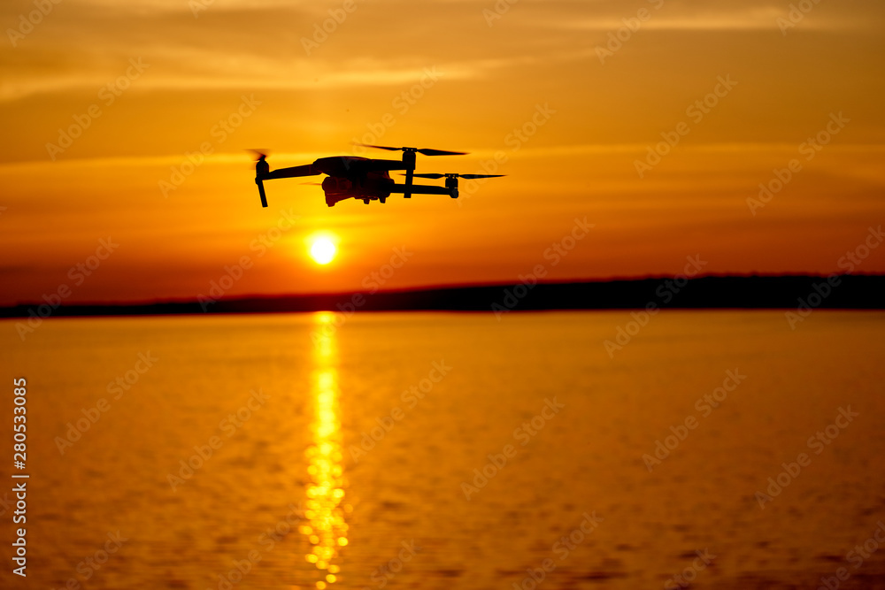 带数码相机的无人机四旋翼机在日落时飞行。美丽的日落在河上