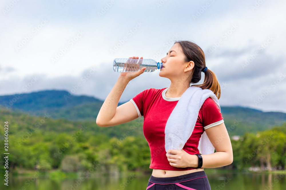 Beautiful Asian athlete woman drinking water during her break from morning  exercise at a lake park 