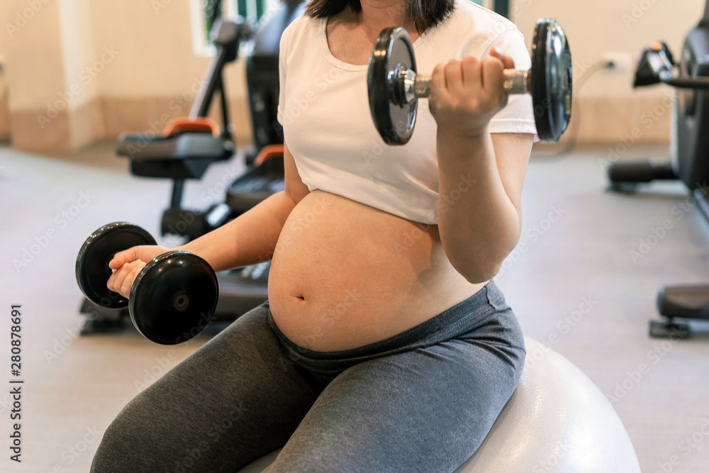 Active pregnant woman exercise in fitness center at yoga room. The young expecting mother holding ba