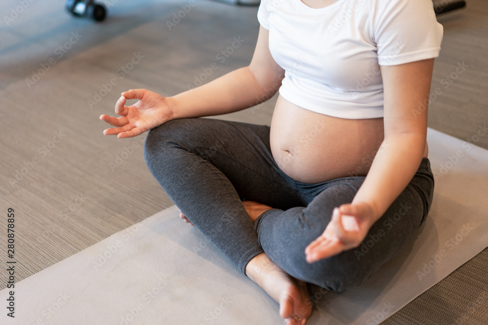 活跃的孕妇在瑜伽室的健身中心锻炼。年轻的准妈妈抱着ba