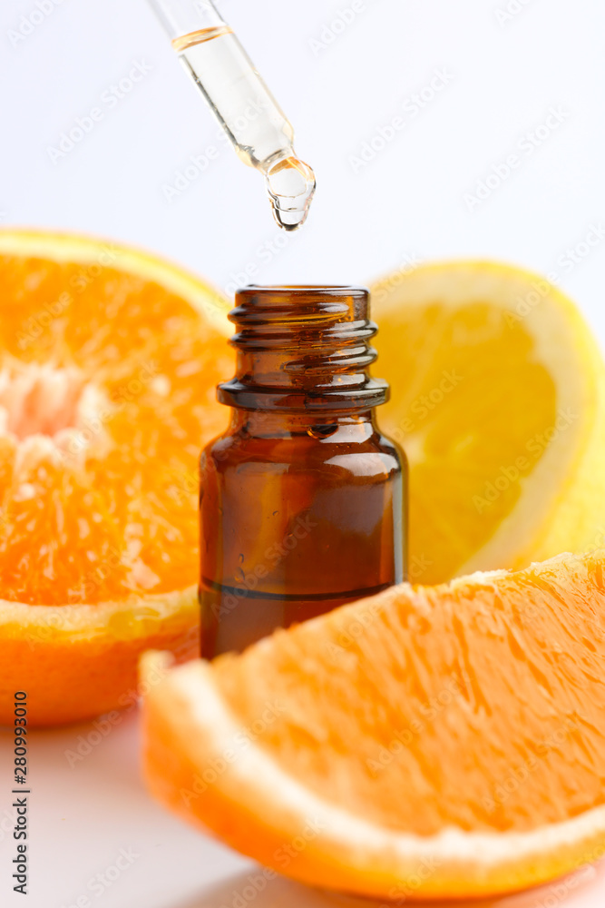 Citrus essential oil dripping from pipette into bottle on white background