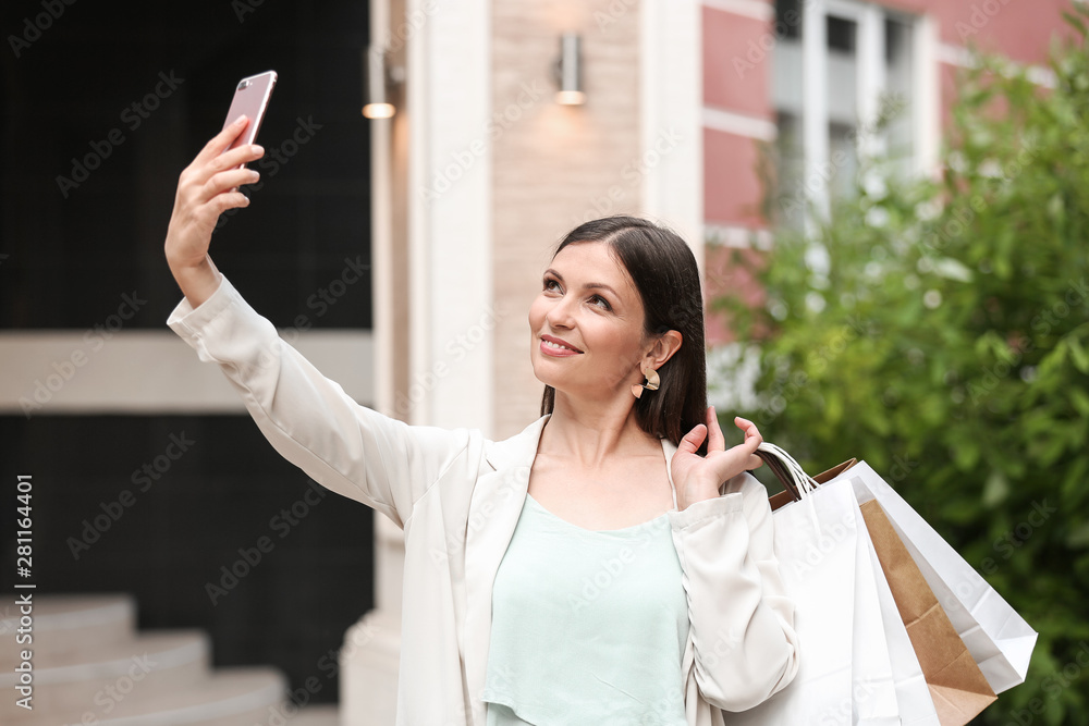 Beautiful woman with shopping bags taking selfie outdoors