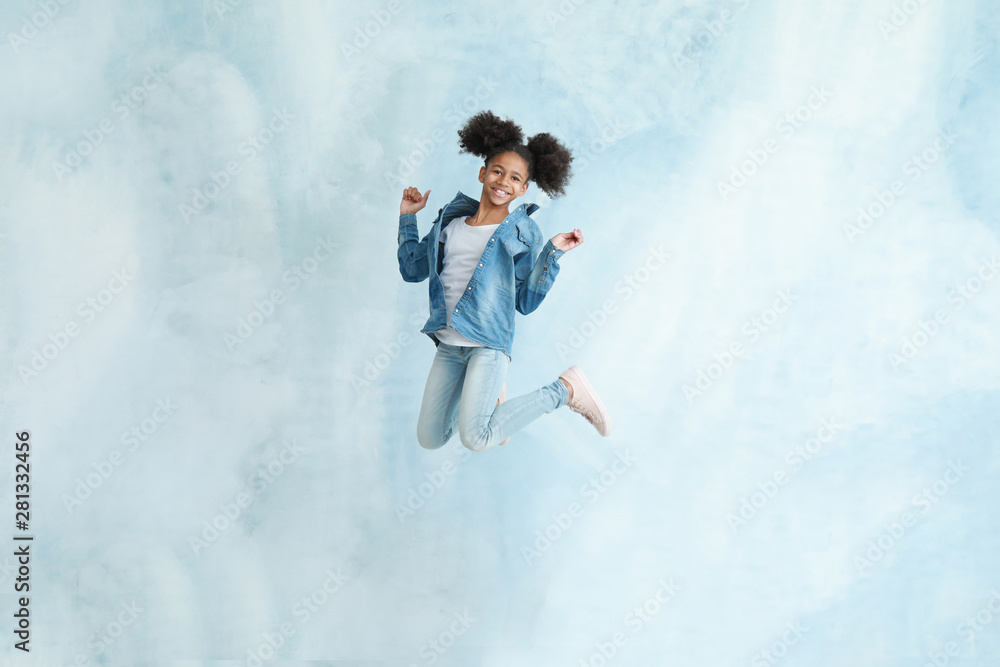 Jumping African-American girl in jeans clothes on color background