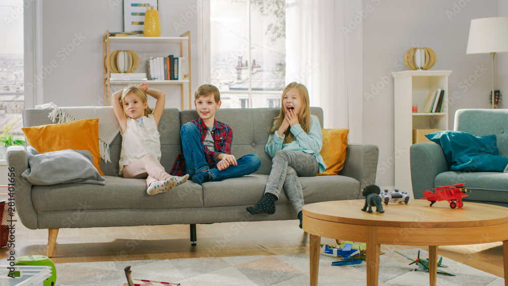 两个可爱的小女孩和一个年轻可爱的男孩坐在沙发上看电视。三件事