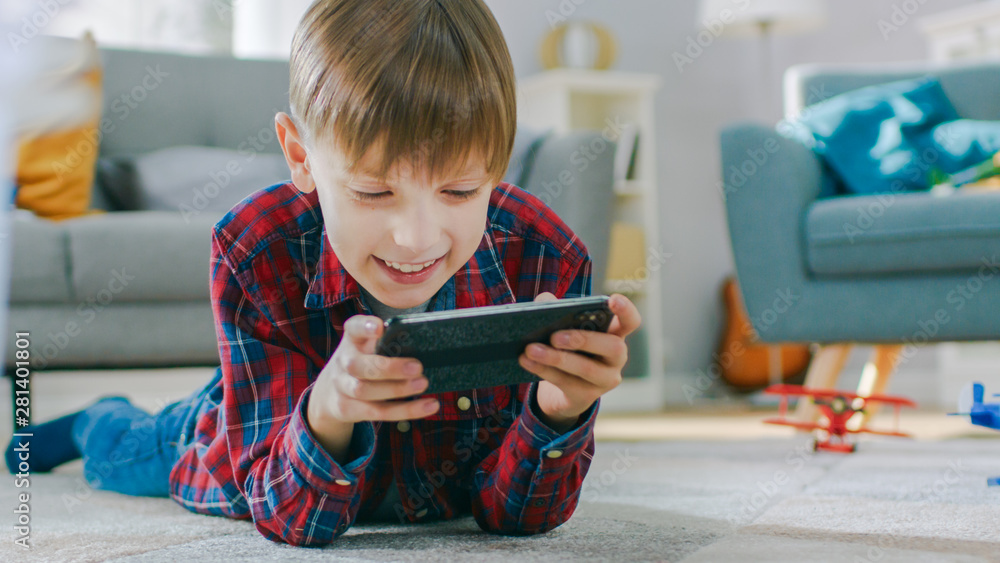 躺在地毯上的聪明小男孩用智能手机玩电子游戏，手里拿着手机