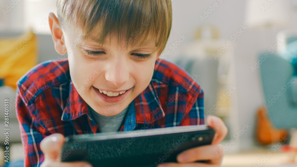 躺在地毯上的聪明小男孩在智能手机上玩电子游戏的特写肖像，Ho