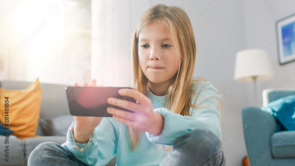 一个聪明可爱的女孩坐在地毯上用智能手机玩电子游戏的人像照片，等等