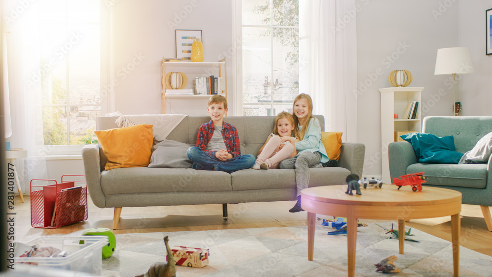 两个可爱的小女孩和一个年轻可爱的男孩坐在沙发上看电视。快乐的孩子