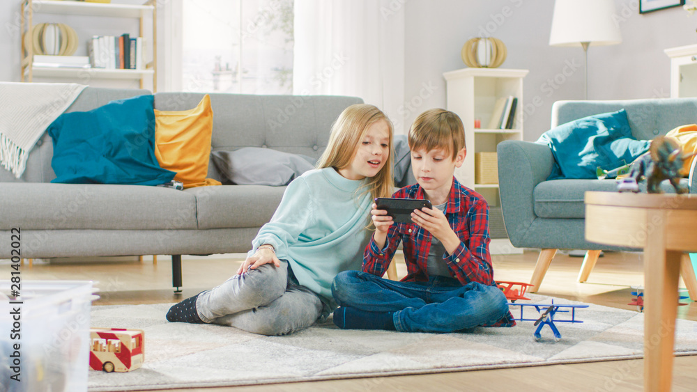 在家：可爱的小女孩和可爱的男孩在智能手机上玩电子游戏，男孩拿着手机