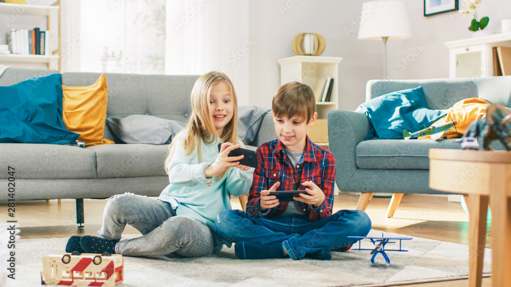 在家里坐在地毯上：可爱的小女孩和可爱的男孩在两人之间玩竞技电子游戏