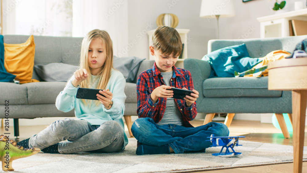 在家坐在地毯上：可爱的小女孩和可爱的男孩在双人竞技电子游戏中玩耍