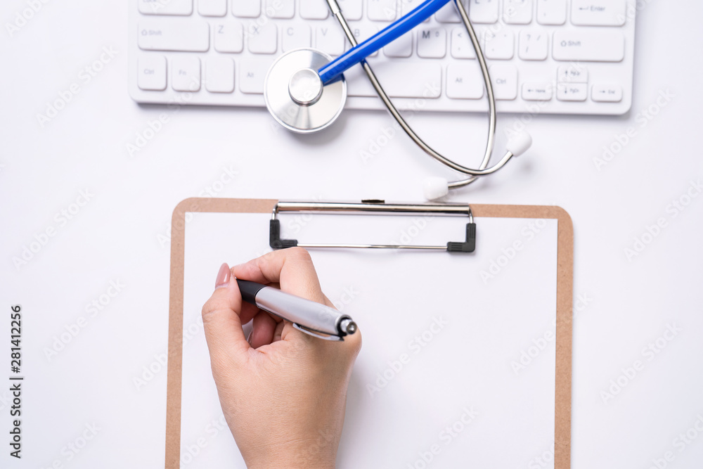 女医生用听诊器在白色工作台上的剪贴板上写病历。