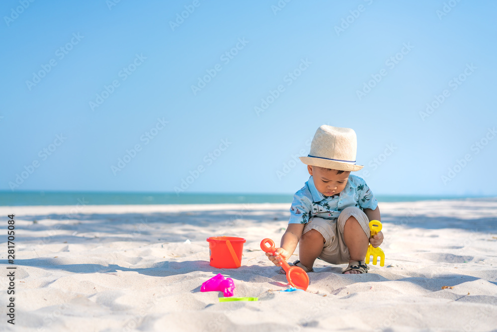 亚洲两岁幼童在海滩上玩沙滩玩具。