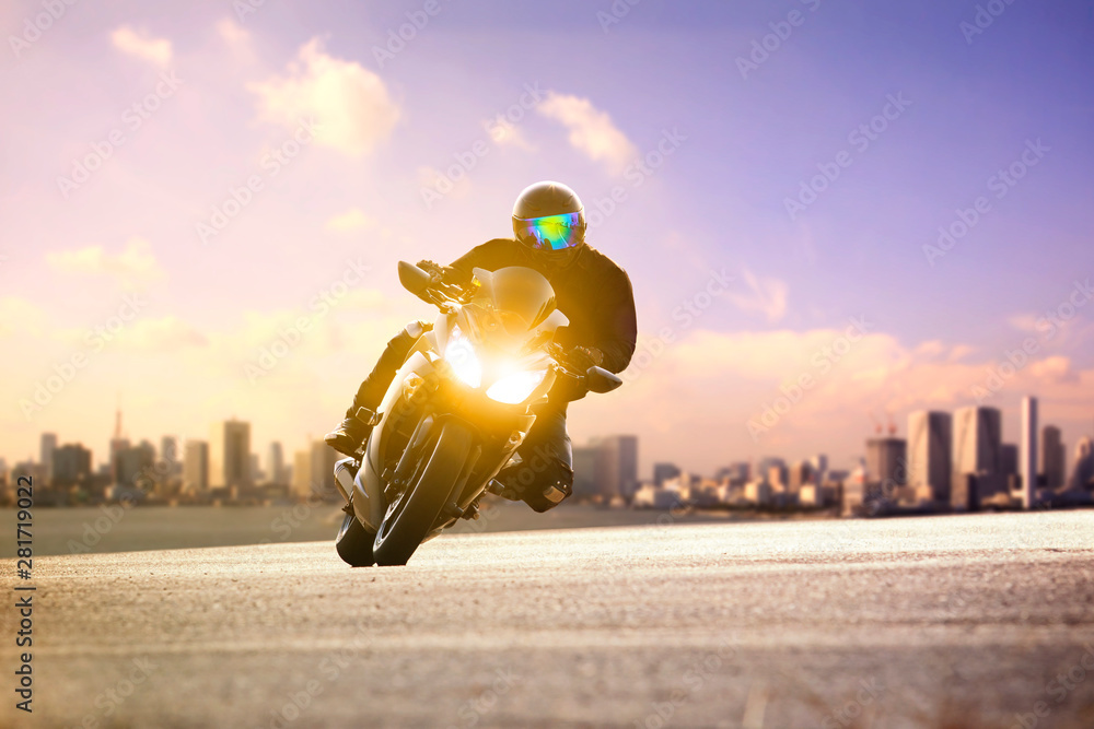 男子骑运动摩托车在城市天际线背景下靠在弯道上