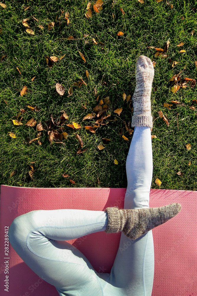 Yoga girl in autumn park with yoga mat on green carpet with fallen yellow leaves. Funny autumn legs 