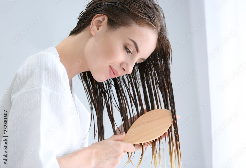 Beautiful young woman brushing hair after washing at home