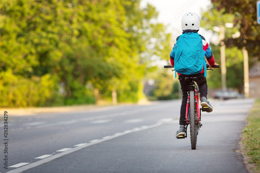 背着帆布背包的孩子在学校附近的公园里骑自行车