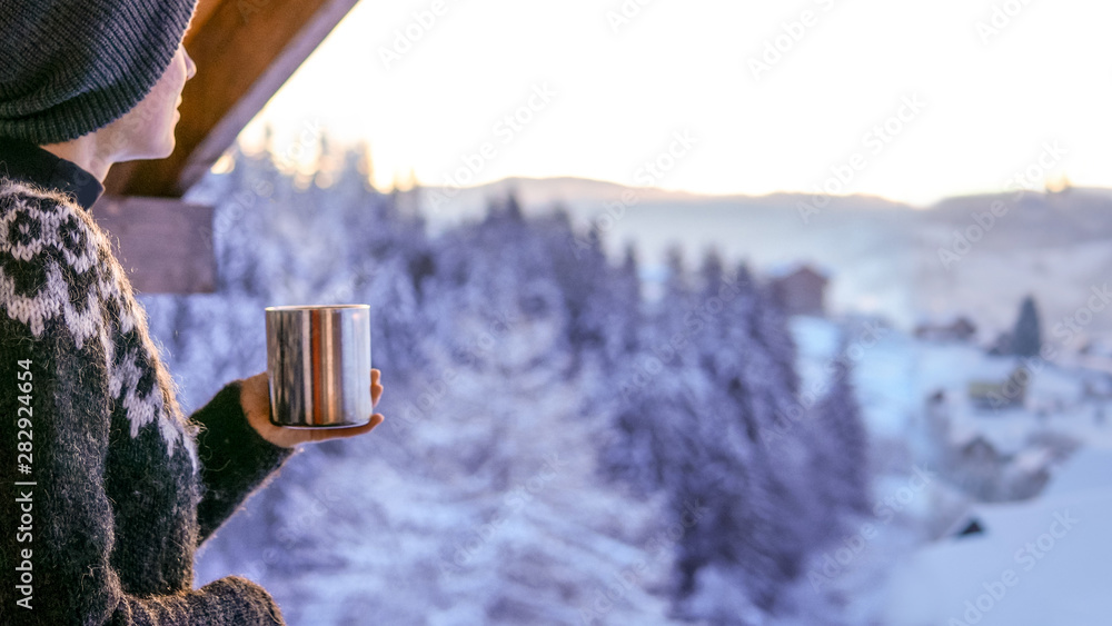 年轻女子喝着咖啡，欣赏冬季的山脉景观