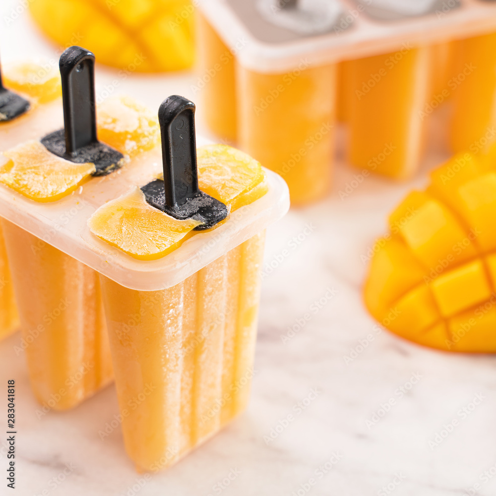 新鲜芒果果冰棍冰放在明亮大理石桌子上的塑料成型盒中。夏日心情概念