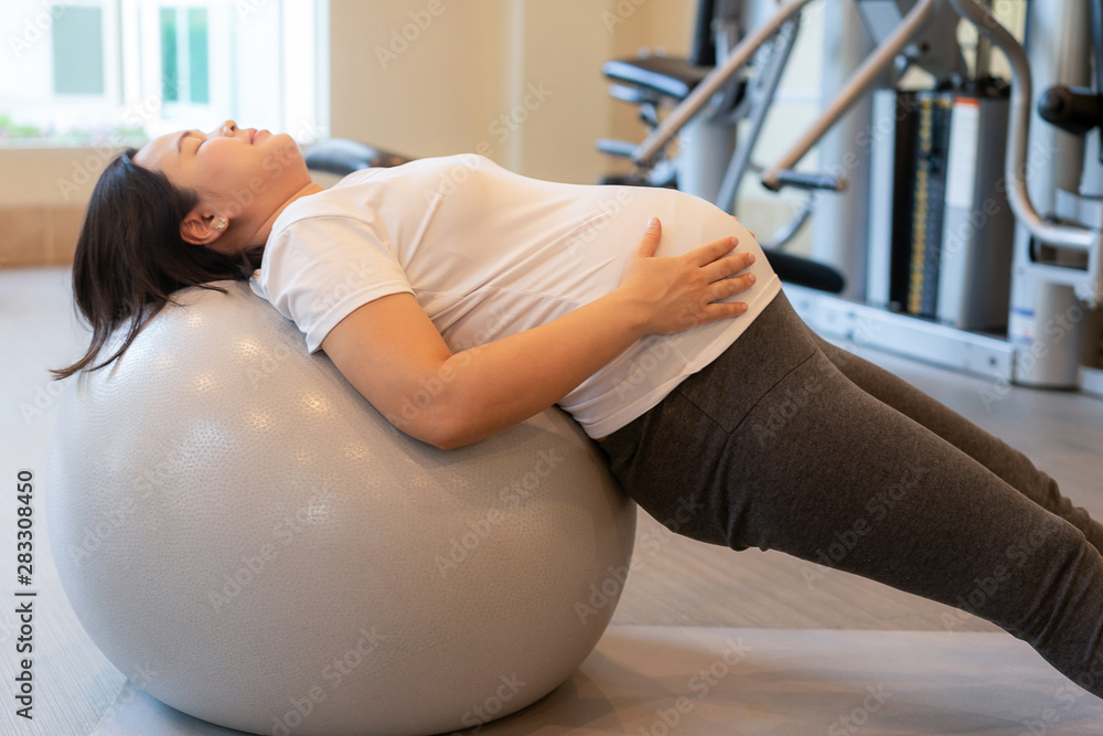 活跃的孕妇在瑜伽室的健身中心锻炼。年轻的孕妇抱着ba