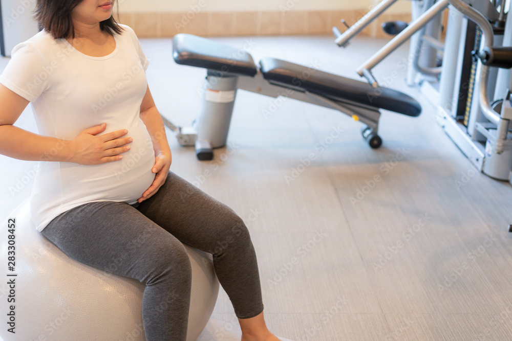 活跃的孕妇在瑜伽室的健身中心锻炼。年轻的准妈妈抱着ba