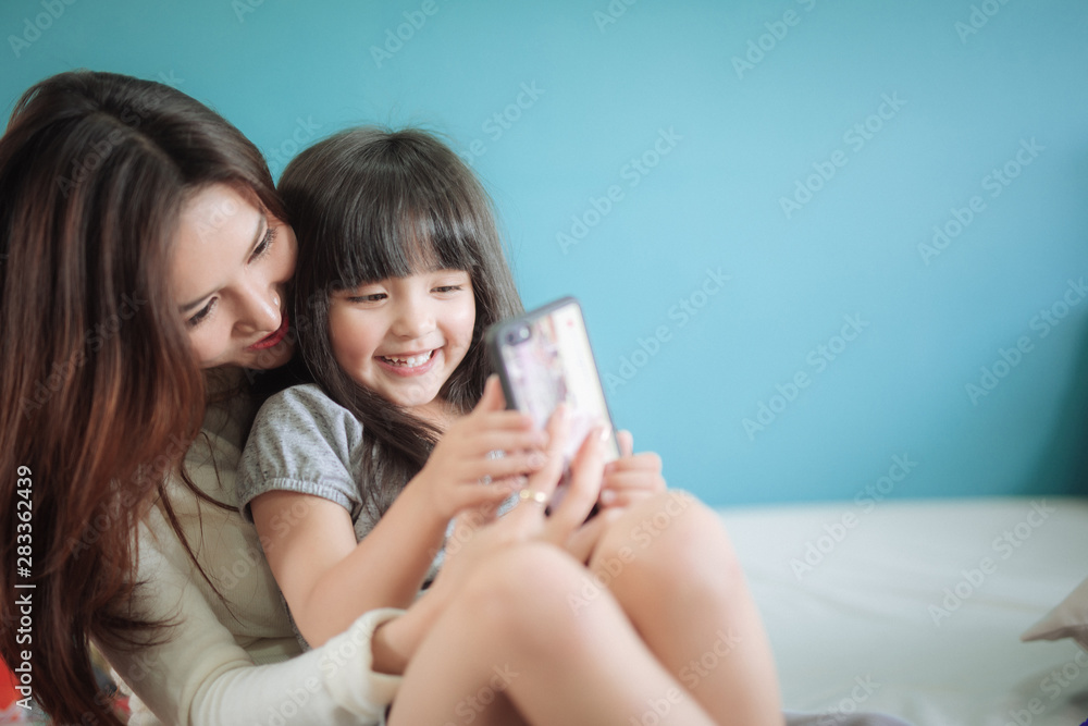 肖像快乐的女儿与母亲玩智能手机