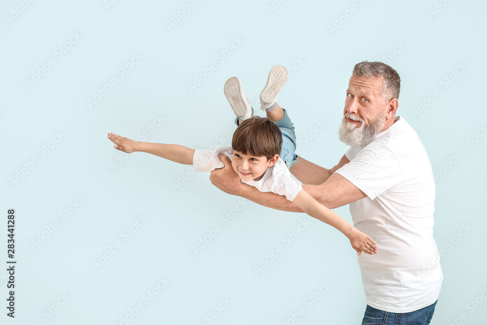 Cute little boy playing with grandfather on light background