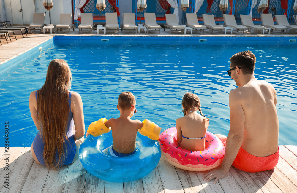 年轻的一家人坐在游泳池附近，后视