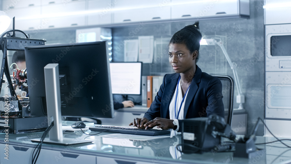 黑人女科学家在研究中心与同事一起在电脑上工作。