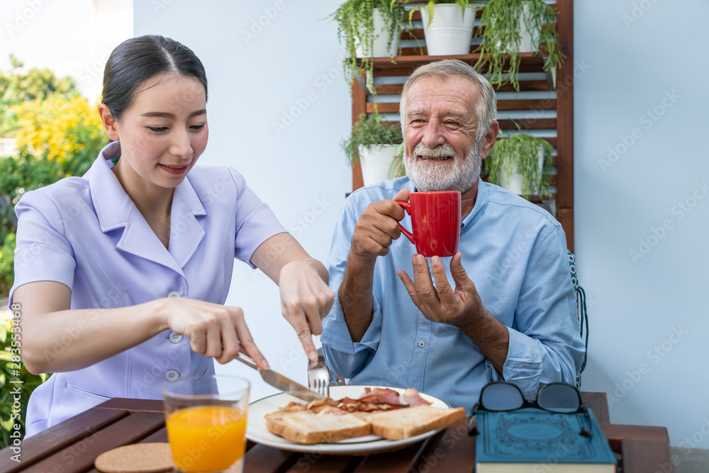 护士在养老院协助老年老人用杯子吃早餐和喝咖啡