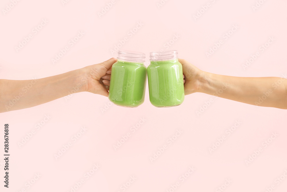 Female hands with tasty green smoothie in mason jars on color background
