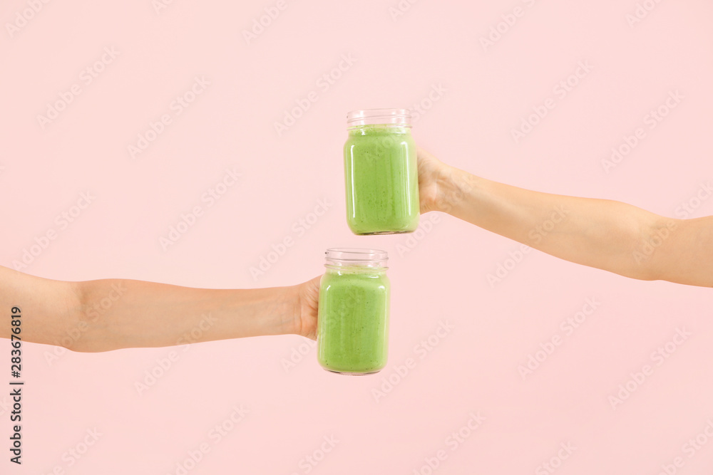 女性手拿美味的绿色奶昔，装在彩色背景的泥瓦匠罐子里