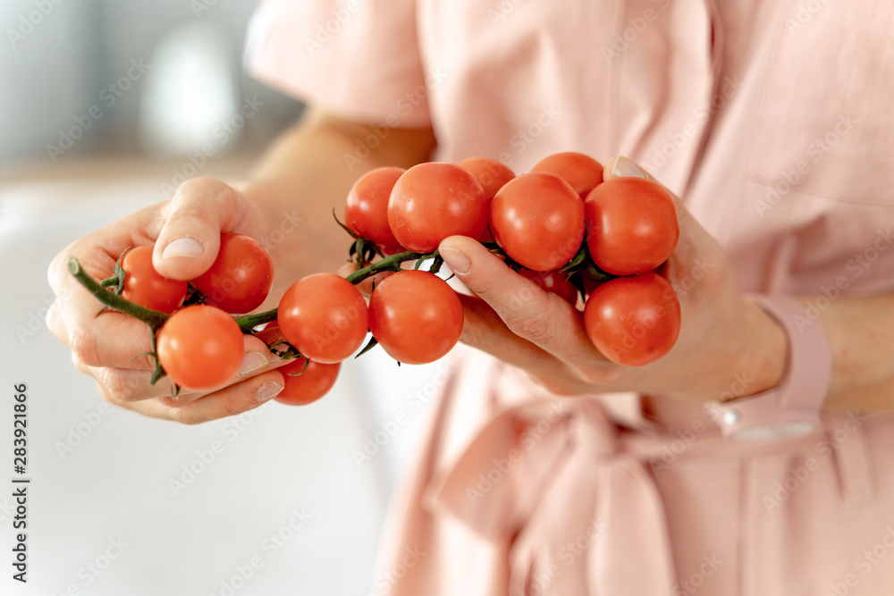 Woman holding twig of ripe cherry tomatoes in the kitchen. Concept of healthy eating and dieting lif