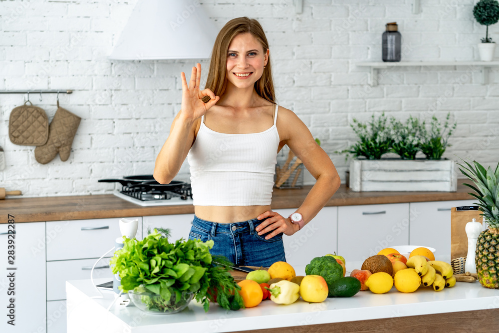年轻女子站在厨房里，周围是混合的新鲜蔬菜，面带微笑，看着镜头