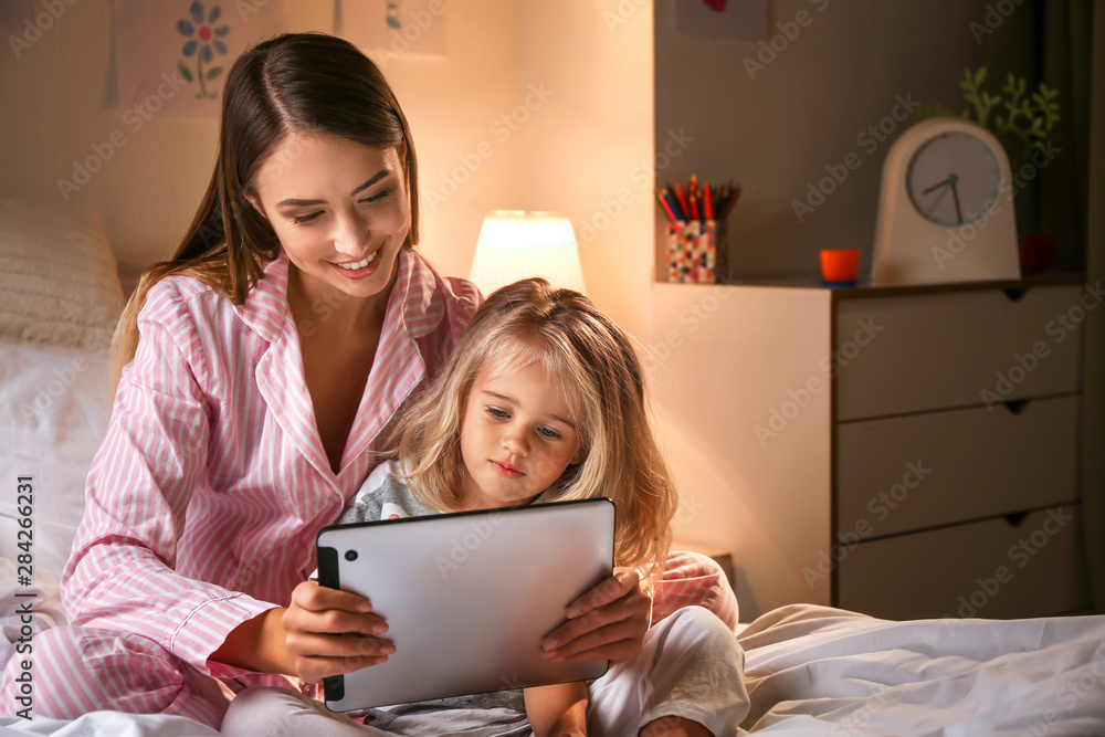 快乐的女人和她的小女儿晚上在床上玩平板电脑