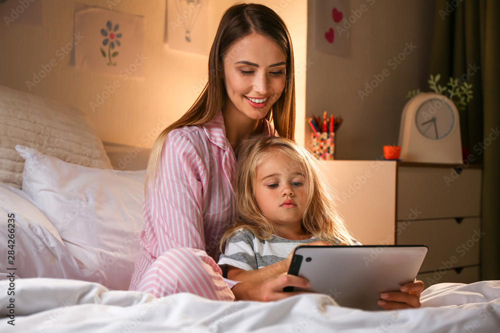 快乐的女人和她的小女儿晚上躺在床上用平板电脑