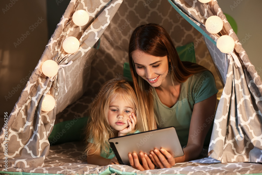 幸福的女人和她的小女儿在家里的小屋里用平板电脑