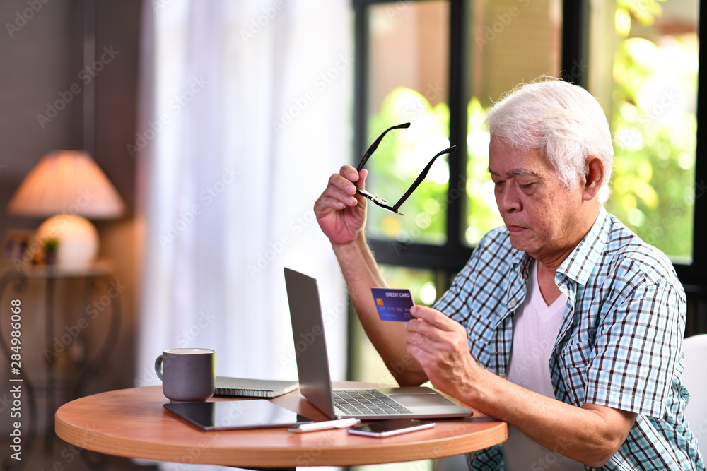 亚洲老年男子使用信用卡网上购物时看起来很困惑