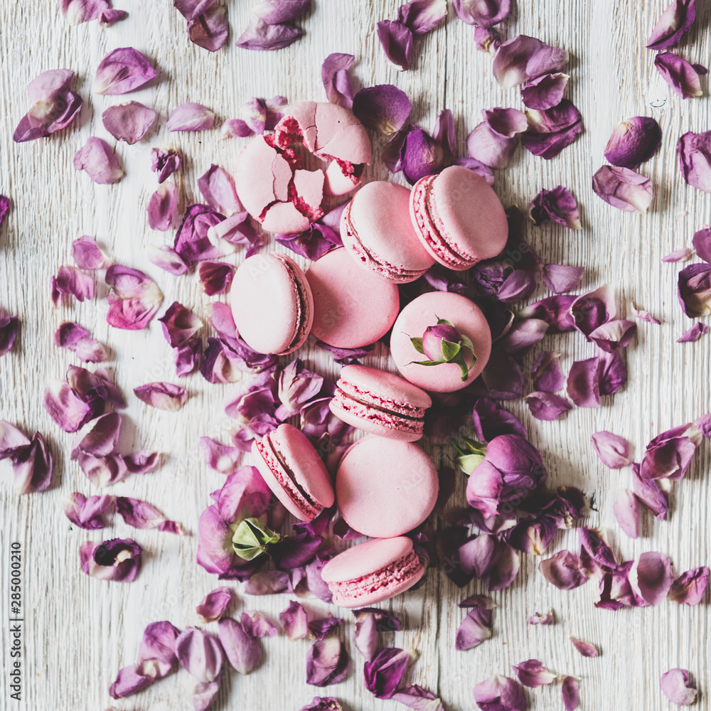 木质背景上的甜粉色马卡龙饼干、玫瑰花蕾和花瓣，俯视图，平方米