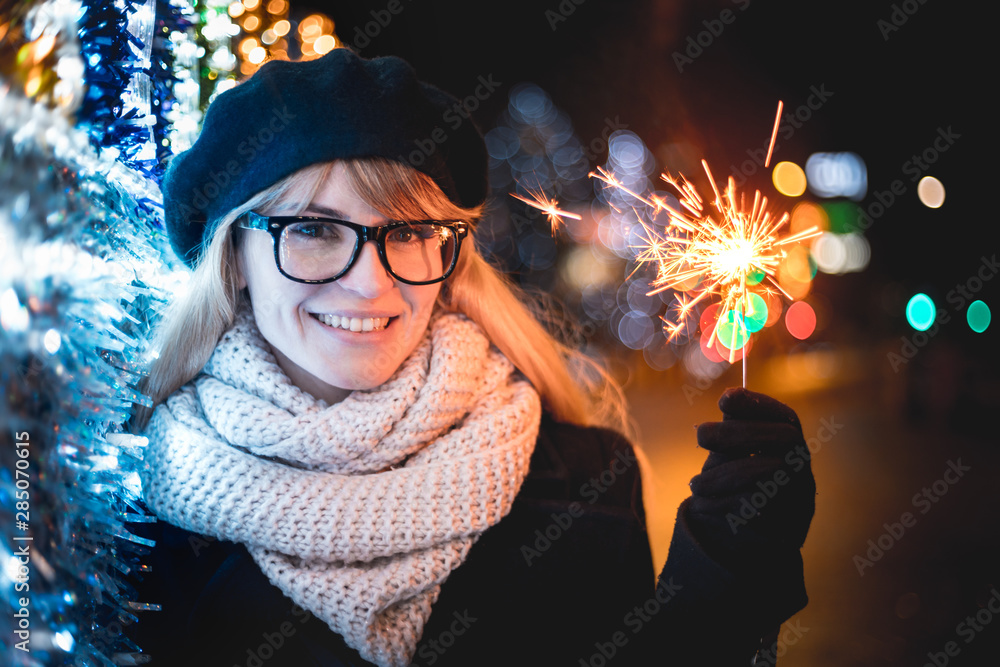 圣诞节或新年期间，快乐微笑的女孩站在明亮的城市街道上，手里拿着闪闪发光的东西