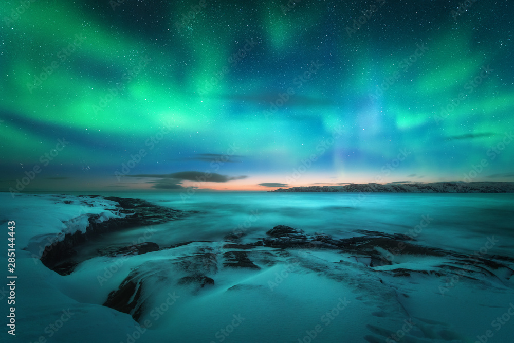 北极光笼罩着岩石海滩和海洋。俄罗斯捷里别尔卡的北极光。波光粼粼的星空