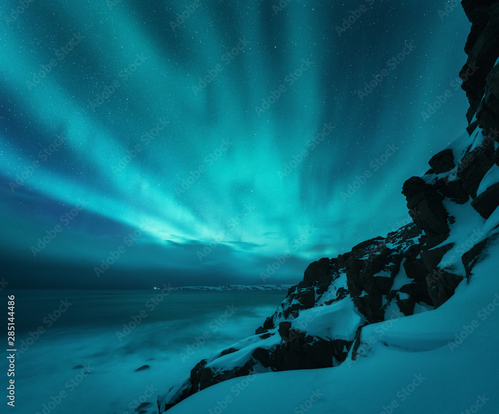 北极光笼罩着岩石海滩和海洋。俄罗斯捷里别尔卡的北极光。波光粼粼的星空