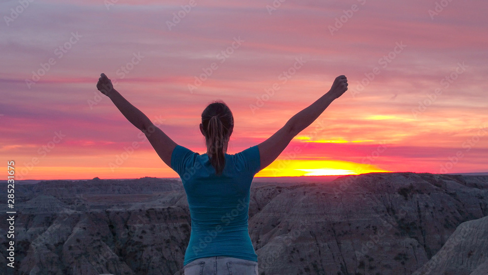 特写：一位快乐的年轻女子在山顶上庆祝粉红色的日落