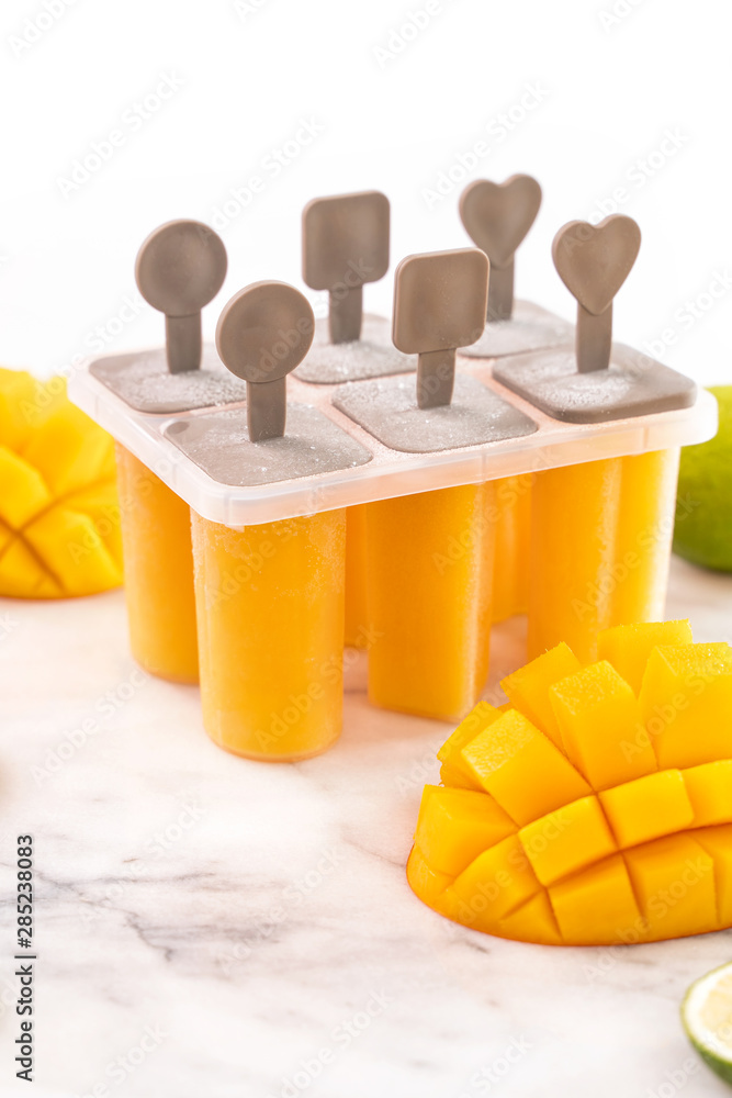 新鲜芒果果冰棍冰放在明亮的大理石桌子上的塑料成型盒里。夏日心情概念