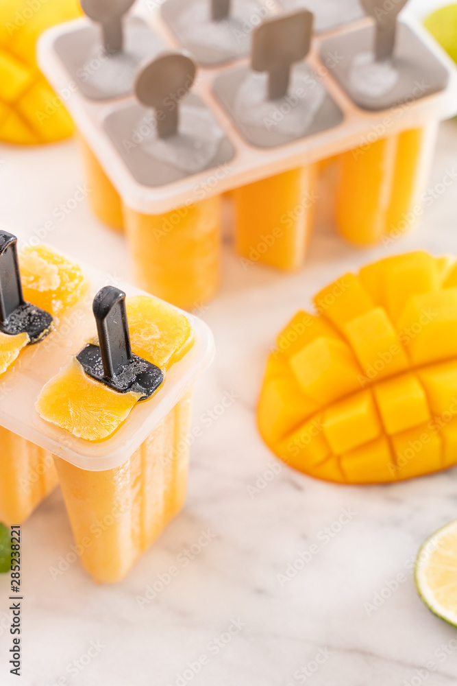 新鲜芒果水果冰棍冰放在明亮的大理石桌子上的塑料成型盒中。夏季心情概念